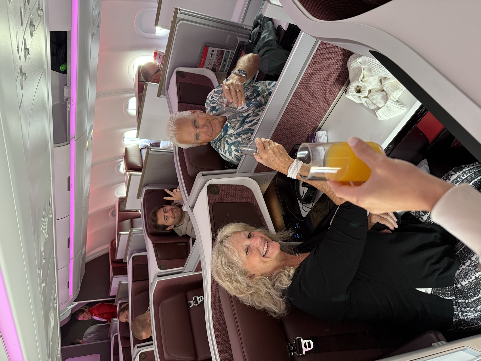 Three travelers smiling and raising their glasses from neighboring premium-cabin seats