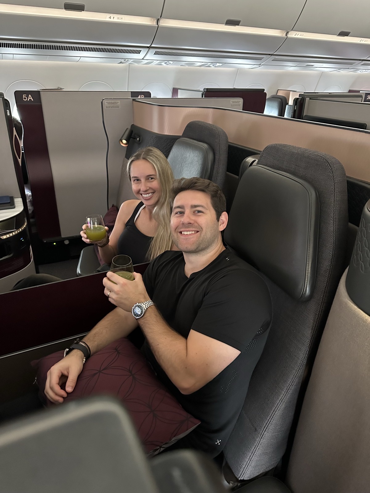 Mike and Christie smiling with drinks in neighboring business-class seats