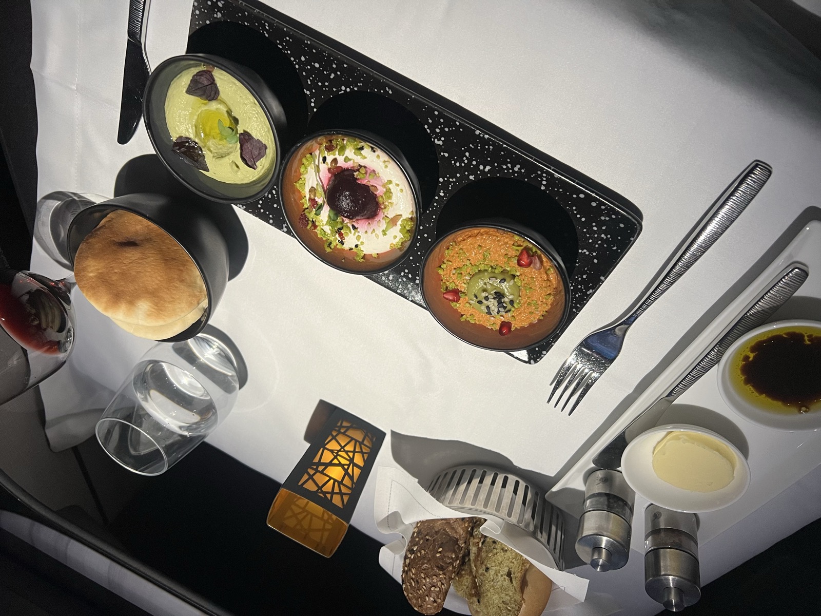 A plated meal with bread, dips, and wine at a premium cabin seat, photographed on our travels